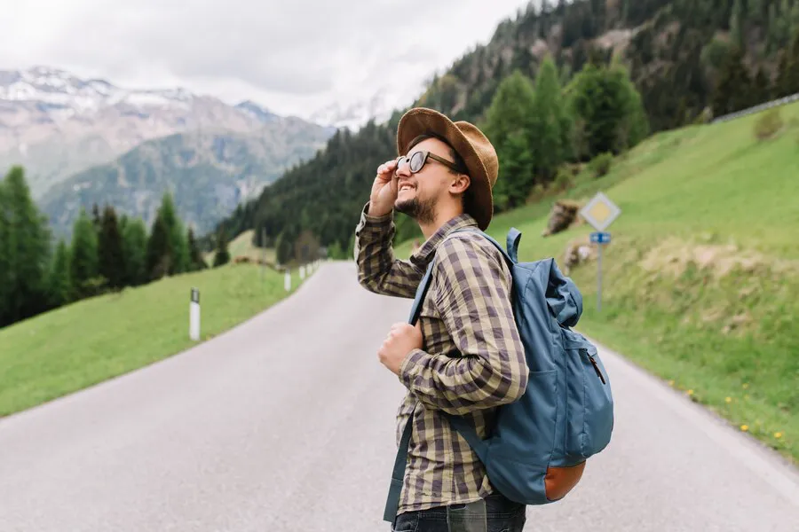 alegre-joven-sombrero-marron-claro-camisa-cuadros-caminando-carretera-campos-hablando-telefono_197531-4383