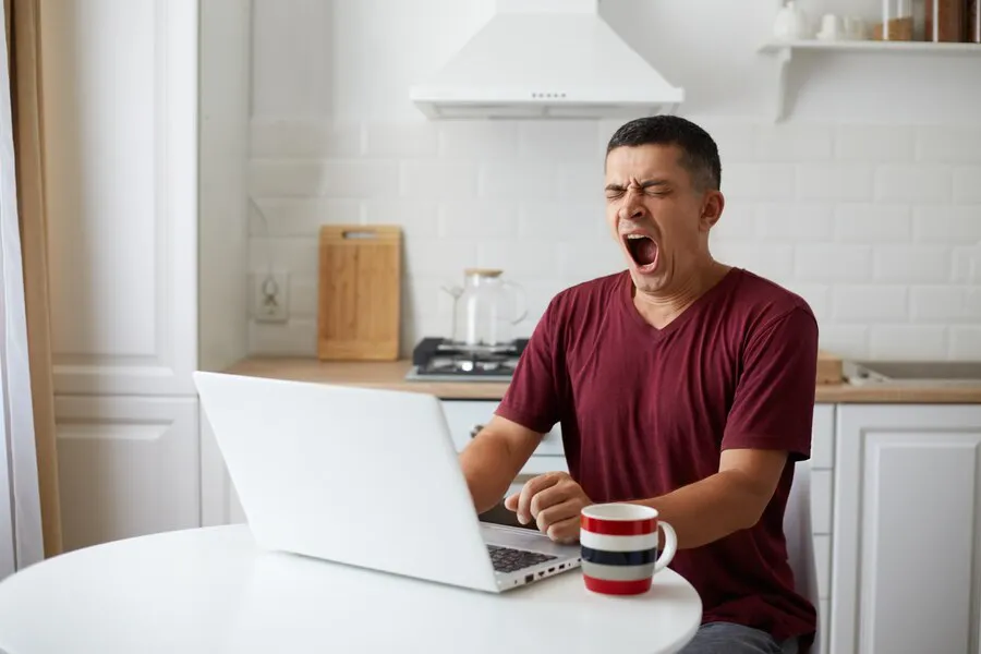 freelancer-hombre-cansado-sentado-mesa-cocina-tener-noche-insomnio-trabajando-linea-bostezando-siente-somnoliento-mirando-cuaderno-tomando-cafe-obtener-energia_176532-15140